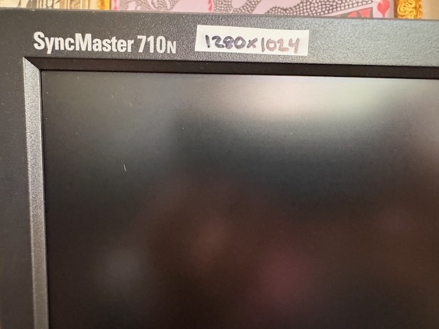 A close up photo of a monitor showing the model name 'SyncMaster 710N', with a white tape label with handwriting indicating the resolution is 1280x1024.